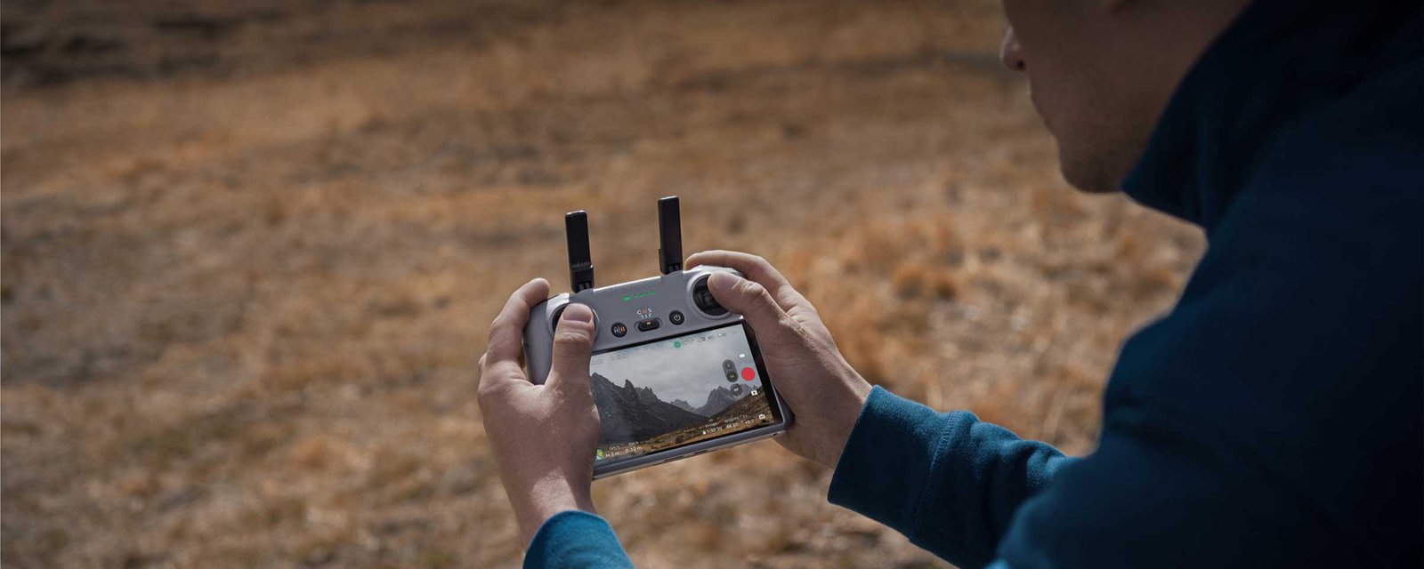 A person holding a DJI remote controller with a live feed displayed on the screen, showcasing a scenic mountain view. The image highlights the DJI Air 3 O4 HD video transmission technology, offering a maximum range of 20 km with enhanced stability and delivering a crisp 1080p/60fps live feed.