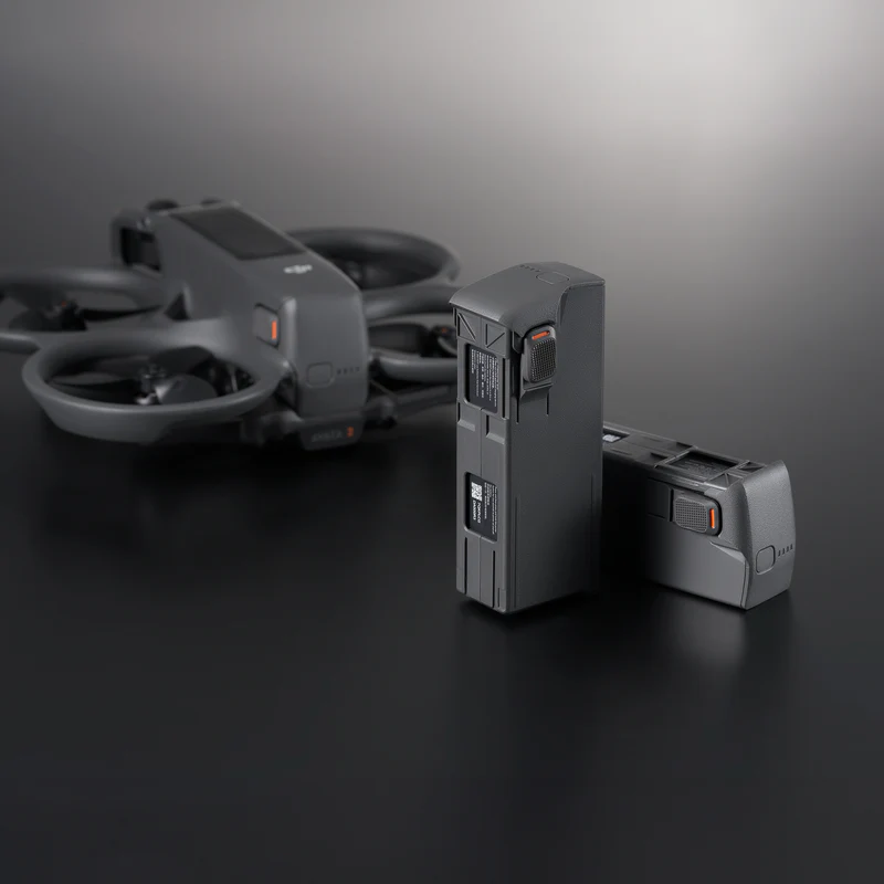 A DJI Avata 2 drone placed on a dark reflective surface, accompanied by two intelligent flight batteries, one standing upright and the other lying flat, highlighting their design and labeling.